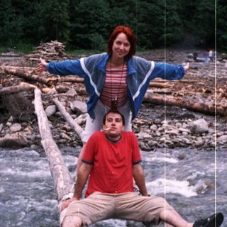 Two people sitting on fallen logs near a river.