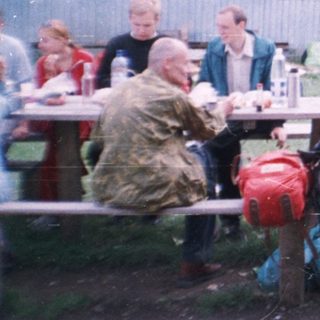Group gathering outdoors at rustic picnic by wooden house.