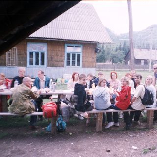 Group gathering outdoors at rustic picnic by wooden house.