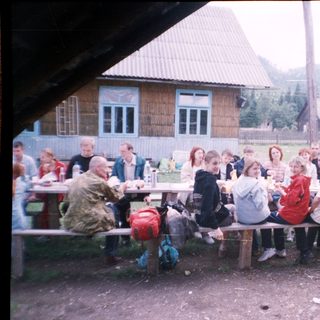 Group gathering outdoors at rustic picnic by wooden house.
