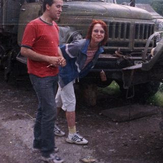 Two people posing beside vintage military trucks.
