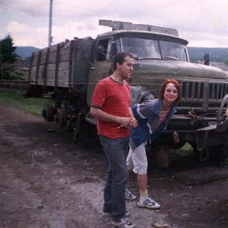 Two people posing beside vintage military trucks.