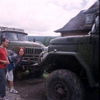 Two people posing beside vintage military trucks.