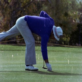 Golfer bending to mark ball on green.