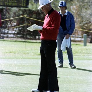 Man in golf attire reading scorecard on green.