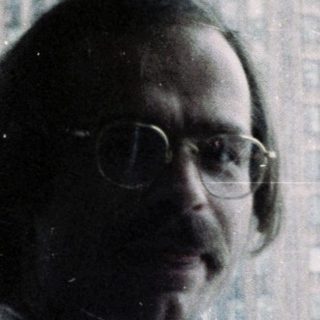 Man in glasses wearing lanyard near city skyline.