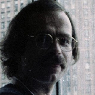 Man in glasses wearing lanyard near city skyline.