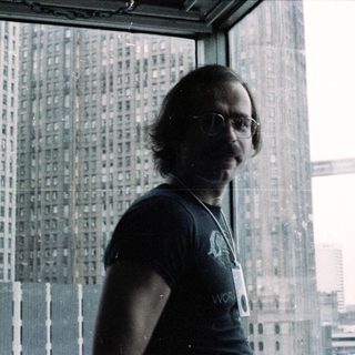 Man in glasses wearing lanyard near city skyline.