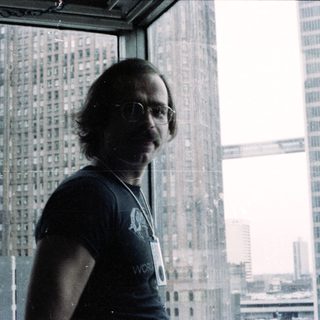 Man in glasses wearing lanyard near city skyline.