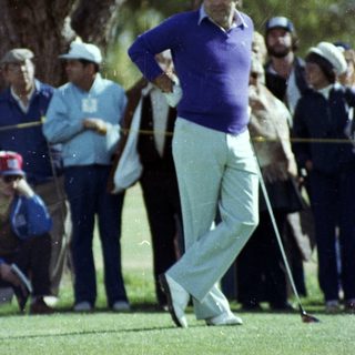 Golfer mid-swing on lush green course.