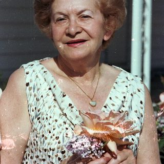 Elderly woman smiling outdoors holding a pastry.