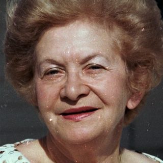 Elderly woman smiling outdoors holding a pastry.