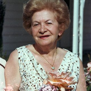 Elderly woman smiling outdoors holding a pastry.