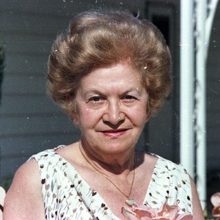 Two elderly people posing outdoors, smiling.