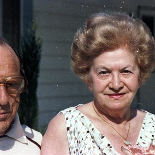 Two elderly people posing outdoors, smiling.