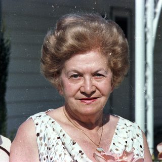 Two elderly people posing outdoors, smiling.