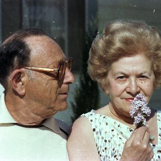 Elderly couple smiling indoors with flowers.