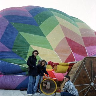 People preparing colorful hot-air balloon on wet ground.