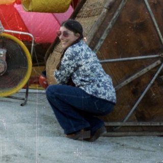 People preparing colorful hot-air balloon on wet ground.
