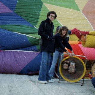 People preparing colorful hot-air balloon on wet ground.