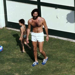 Shirtless man and child playing with ball outside.