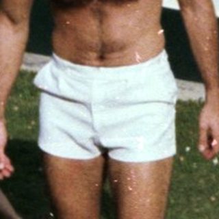 Shirtless man and child playing with ball outside.
