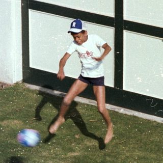 Boy kicking soccer ball outdoors near garage.