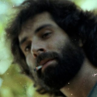 Man smoking outdoors amidst lush green foliage.