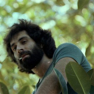 Man smoking outdoors amidst lush green foliage.