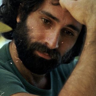 Man resting hand on forehead amidst green foliage.