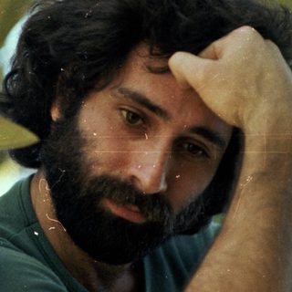 Man resting hand on forehead amidst green foliage.
