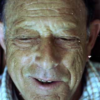 Wet, smiling elderly man with closed eyes.