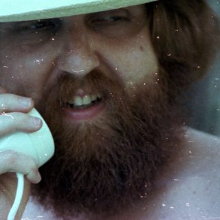 Man in fedora holding phone near water.