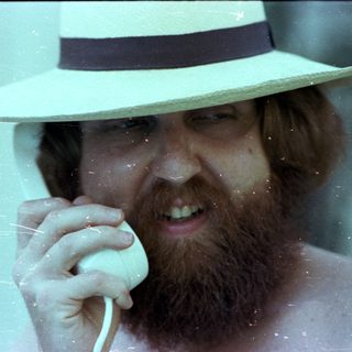 Man in fedora holding phone near water.