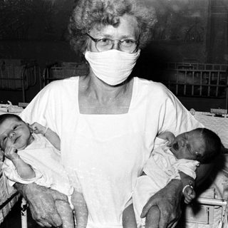 Nurse holding newborns in hospital nursery.