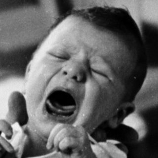 A baby crying while being held by an adult.