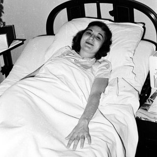 Woman lying in hospital bed, mid-20th century.