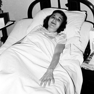 Woman lying in hospital bed, mid-20th century.