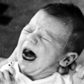 Baby crying while being held by adult.