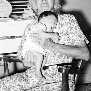 Old woman holding a baby indoors.