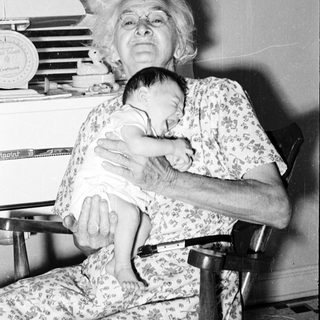 Old woman holding a baby indoors.