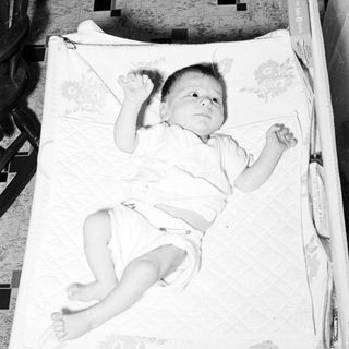 Baby lying on patterned blanket in crib.