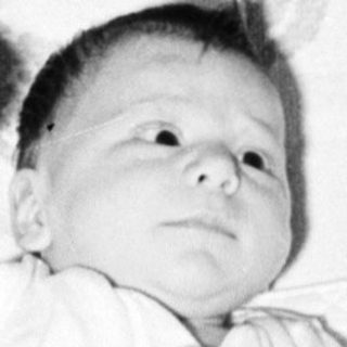 Baby lying on patterned blanket in crib.