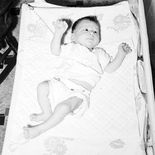 Baby lying on patterned blanket in crib.
