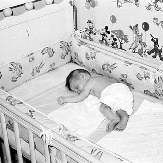 Baby sleeping peacefully in vintage crib with cartoon prints.
