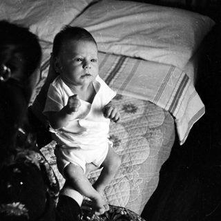 Baby sitting on bed in vintage photograph.