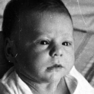 Baby sitting on bed in vintage photograph.