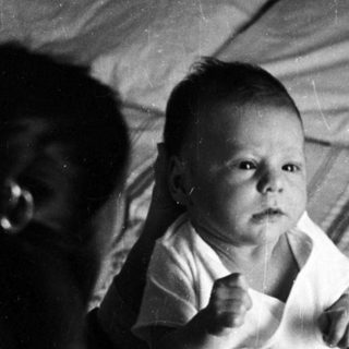 Baby sitting on bed in vintage photograph.