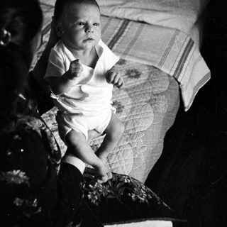 Baby sitting on bed in vintage photograph.