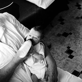 A person gently feeds a baby in bed.